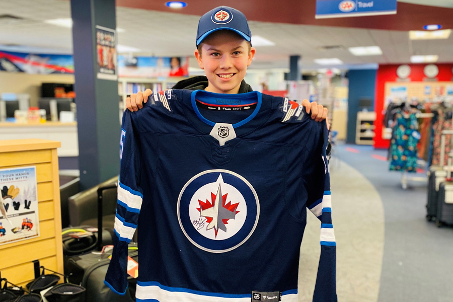 Image showing young boy holding up a Winnipeg Jets hockey jersey and smiling.