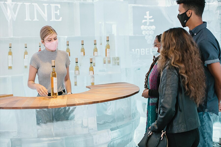 Image showing woman wearing a face mask displaying wine bar wares to customers also wearing face masks.