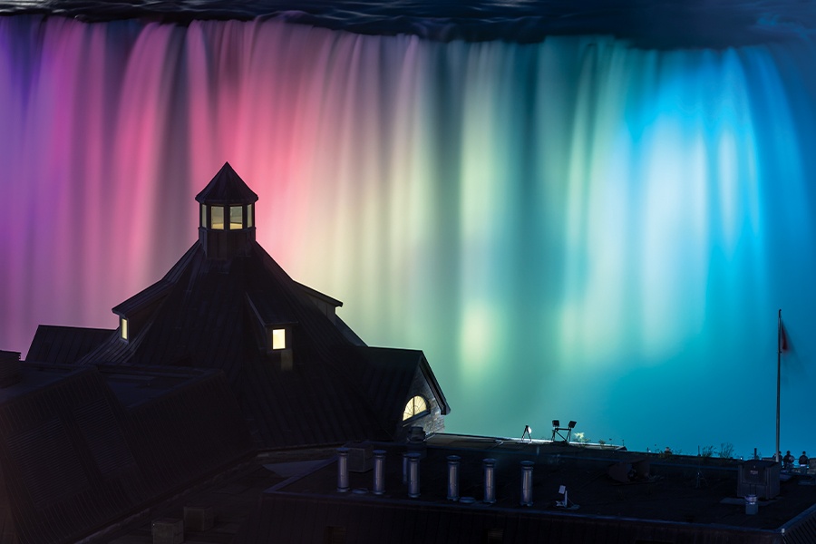 Image showing Niagara Falls at night lit up by artificial lighting and a building in silhouette in the foreground.