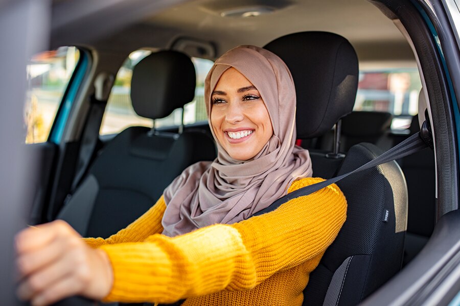 Image showing a young woman wearing an orange sweater behind the wheel of a car and smiling.