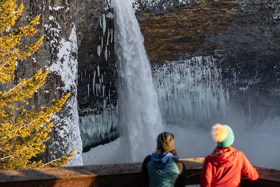 Images showing a couple standing in front of a partially frozen waterfall in the mountains.