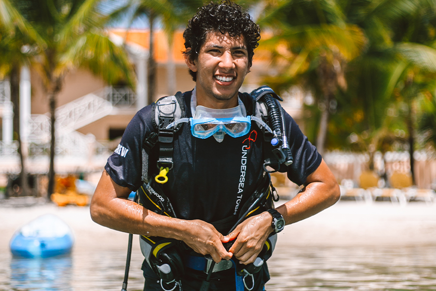 Image showing a young man in waist deep water suiting up with scuba diving gear.