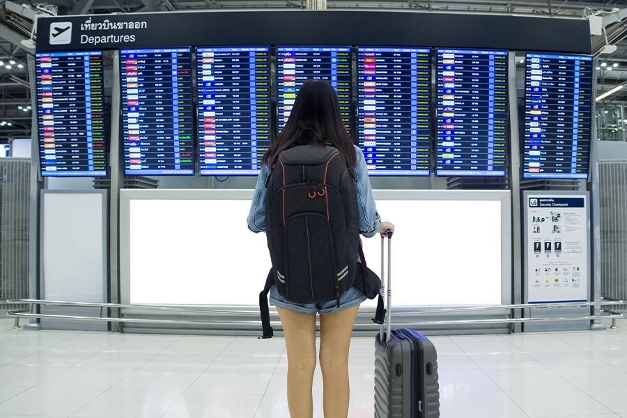 Image of a young woman standing with her luggage looking at an airport departures and arrivals screen.