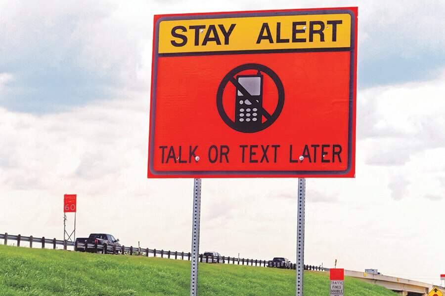 Image showing a yellow and red road sign beside a highway with words reading: Stay Alert Talk or Text Later.