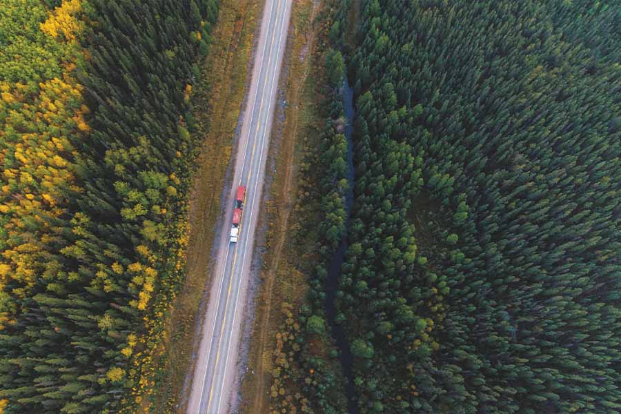 Image showing overhead view of highway below with a white truck towing a red trailer through a forested region.