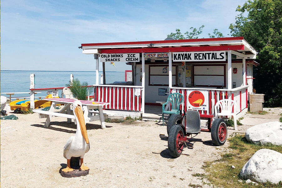 Image showing small building in background with sign reading Kayak rentals, with picnic table and pelican statue in foreground.