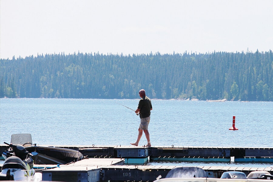 Image showing man walking along wooden dock with a fishing rod in his hand.