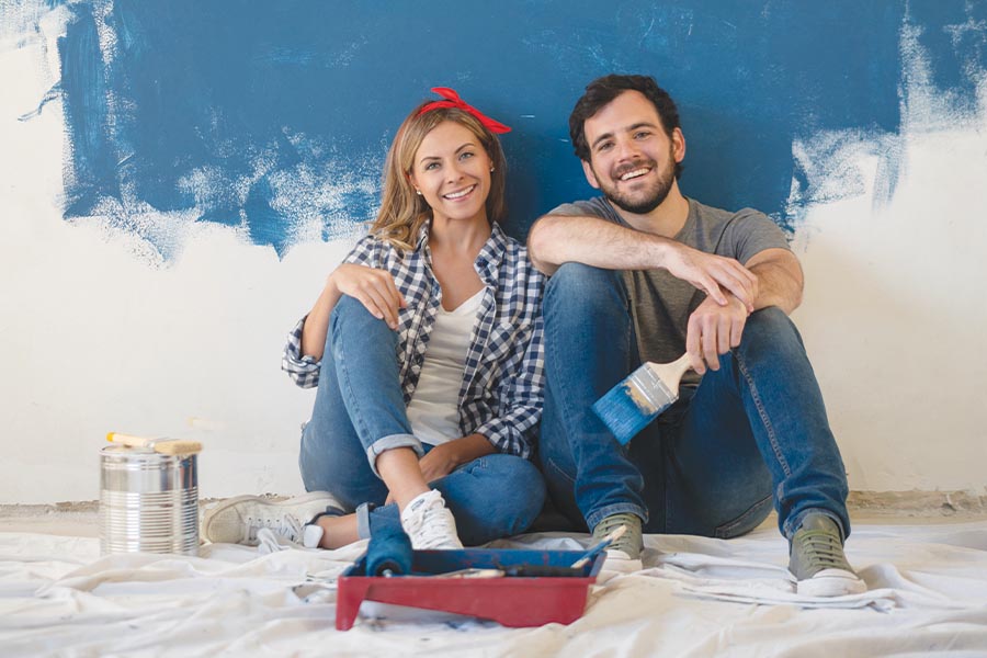 Image showing young couple with paintbrushes sitting in a partly painted room and smiling at the camera.