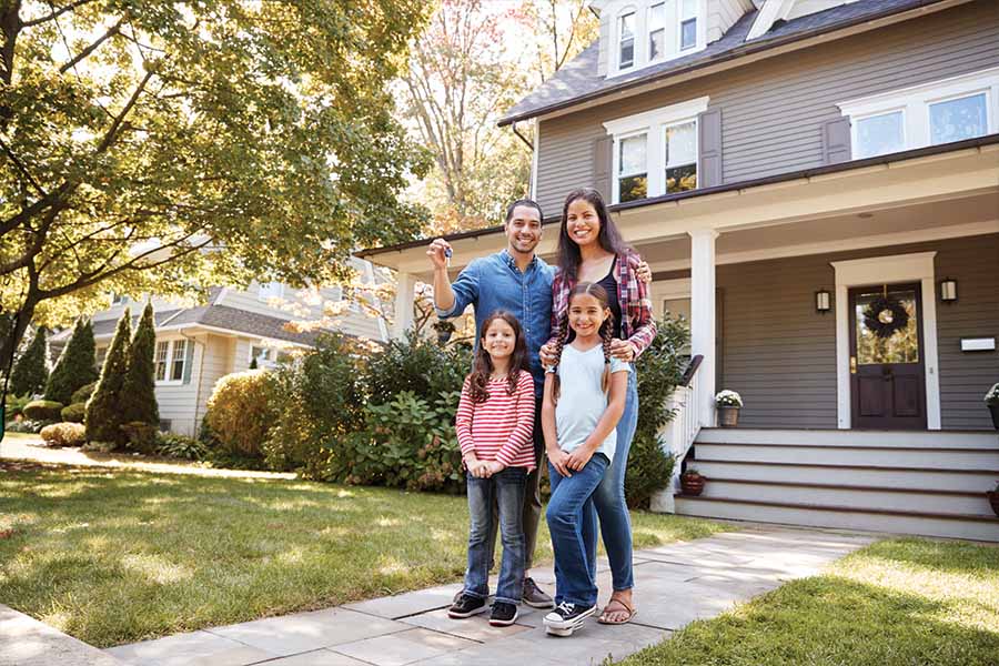Image showing Mom, Dad and two daughters smiling at the camera while standing outside a suburban home in a well-treed neighbourhood.