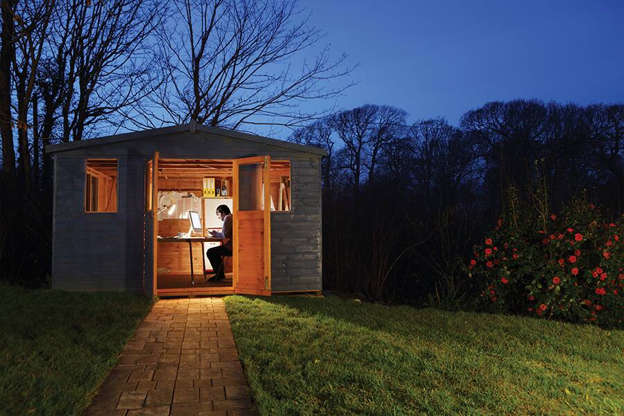 Nightime image showing a man sitting inside a medium-sized shed being used as a backyard office.