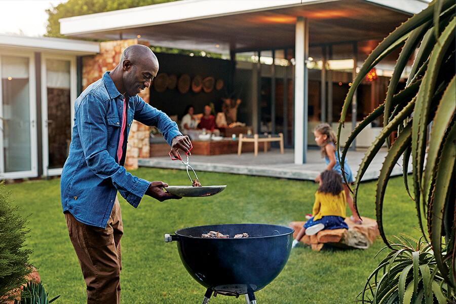 Image showing a man cooking with his backyard barbecue while two children play in the background.