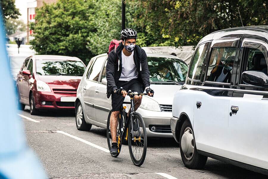 Image showing a bicyclist wearing a face mask and helmet riding beside a lineup of cars.