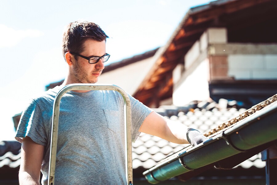 Image showing a man up a ladder cleaning his house eavestroughs.