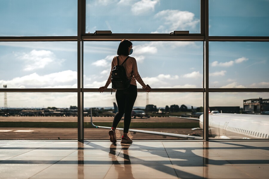 Image showing a young woman wearing a backpack and staring wistfully out a window overlooking an airport tarmac.