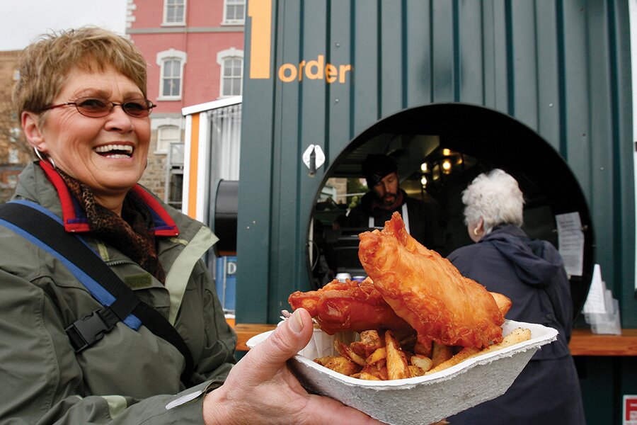 Image showing a woman smiling while holding up a box of golden brown fish and chips.