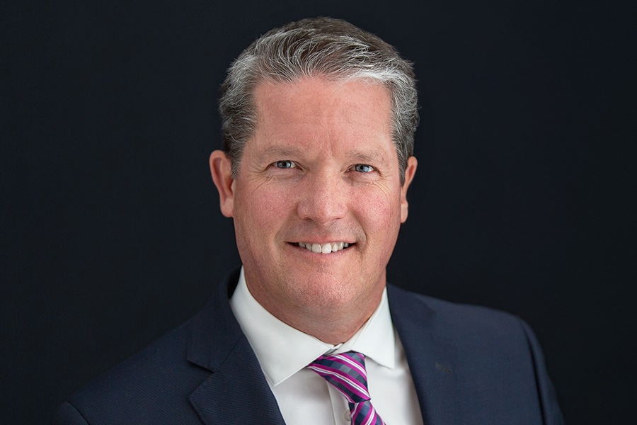 Image showing head-and-shoulders photo of CAA Manitoba CEO Tim Scott smiling in dark suit and purple-white striped tie.