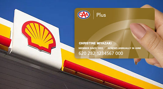 A woman's hand holding a CAA Plus Membership Card with Shell signage in the background.