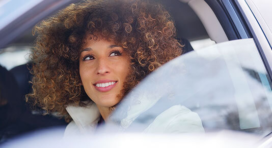 A young black woman sitting inside a vehicle looking out a partially opened window
