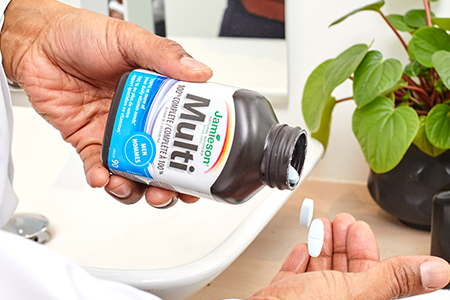 Jamieson image featuring hand holding multi-vitamins bottle with pills spilling into other hand