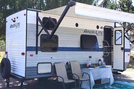 Image showing a medium-sized trailer at a campsite with a small table and chairs set up outside.