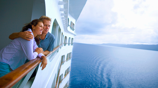 Couple leaning on rail of cruise ship, looking at ocean