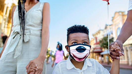 Image showing young boy wearing Mickey Mouse style face mask while holding hands of two adults.