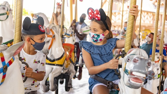 Image showing young boy and girl riding carousel horses while wearing face masks.