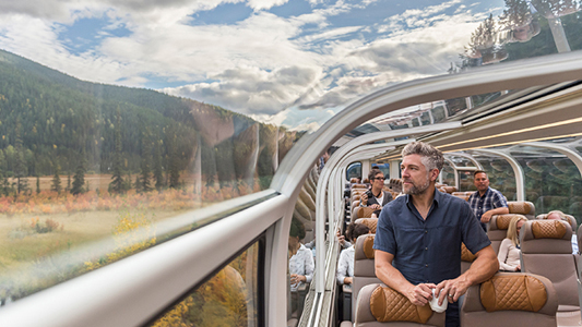 A man looking out a train window at the mountains.