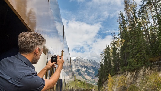 A man taking a picture of the Rocky Mountains out the window of a moving train.