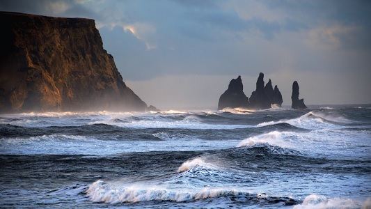 Rough waves in the ocean with rock formations in the background.