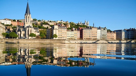 View of French cathedral and other town buildings reflected in the waters of the Rhone River.