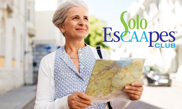 An elderly woman holding a map while walking through a town.