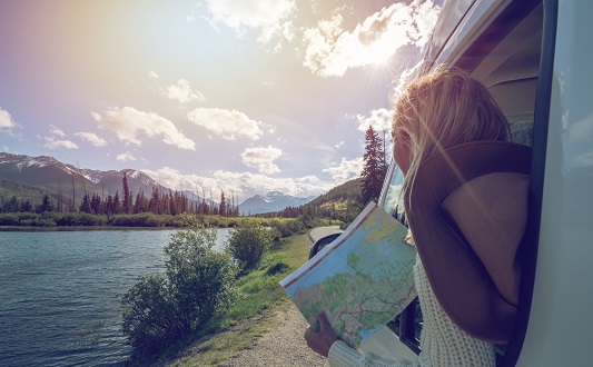 Woman looking out of the car with a map in hands.