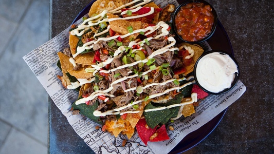 Image showing a tasty-looking plate of nachos with side sauces on a table.