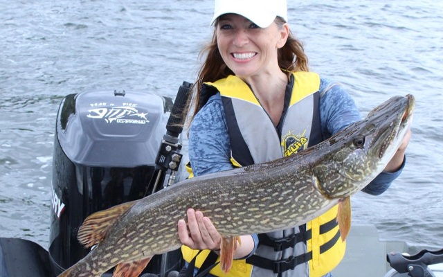 Image showing a young woman standing in a motor boat holding a large fish in her hands.