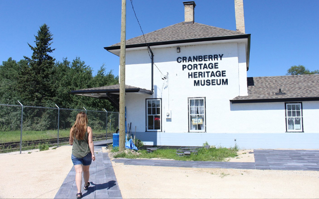 Images showing a woman walking toward a white mid-sized building with the words Cranberry Portage Heritage Museum on front wall.