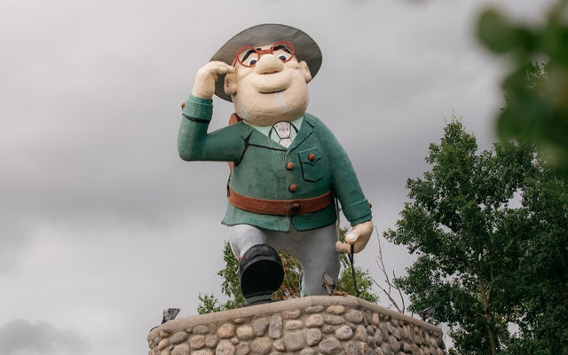 Statue showing a stylized male figure wearing an olive green jacket and hat and wearing red spectacles.