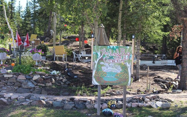 Image showing a sign, a rock lined path and lawn chairs in a forest clearing.