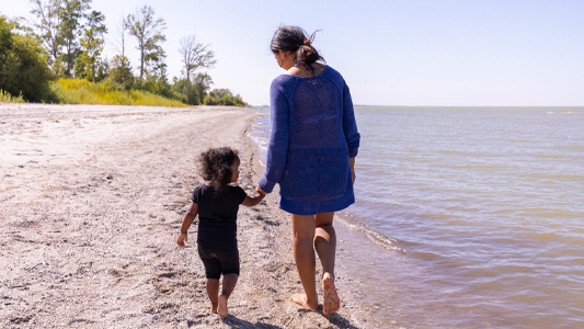 Image showing a woman and a small child walking barefooted on a beach.