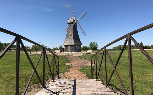 Images showing a small wooden bridge in the foreground with a windmill in the background.