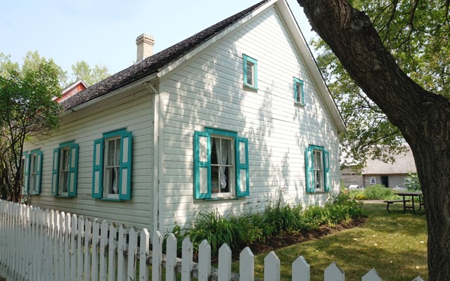 Image showing a small white wooden building with light blue trim on the windows. 