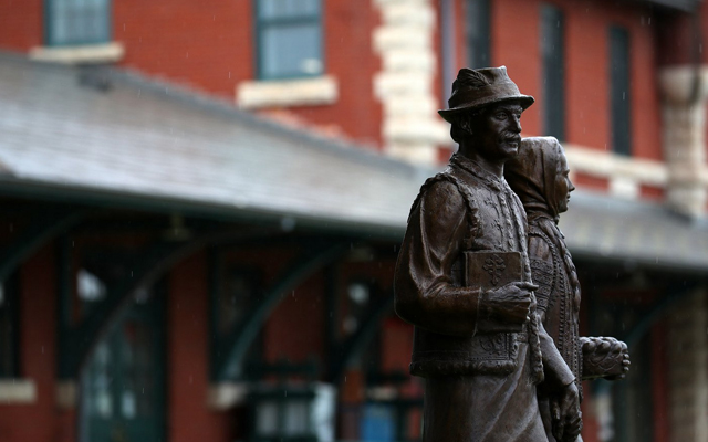 Images showing a statue of two people in the foreground and a red brick building in the background.