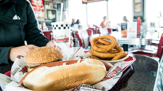 Image showing a plate with a hamburger, a hot dog and onion rings on a table inside a restaurant.