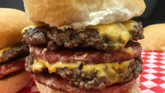 Images showing a closeup view of a double-decker hamburger with melted cheese.