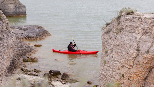 Images showing a kayaker paddling near some rocks on the lake shore.