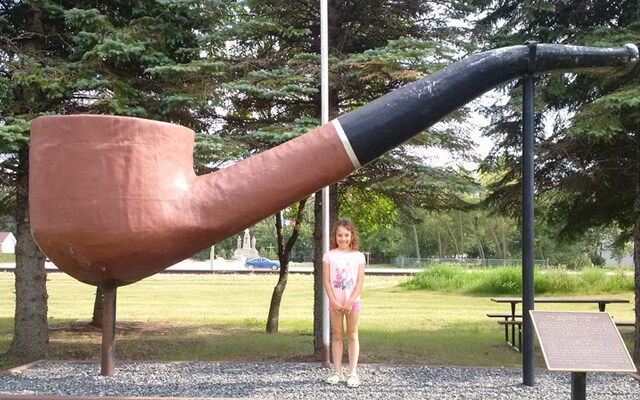 Image showing a young girl standing beside the statue of a giant tobacco pipe.