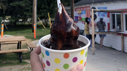 Image showing a closeup of a hand holding an ice cream treat with the ice cream shop in the background.