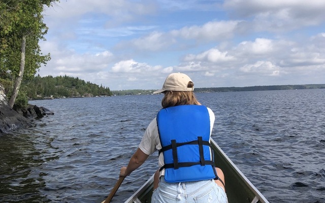 Image showing a woman paddline a canoe on a lake very close to shore.