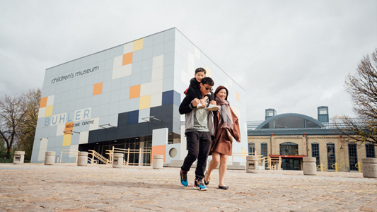 Image showing a couple walking past a multi-coloured building carrying a child.