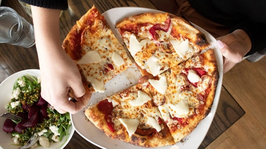 Image showing a hand reaching for a slice of pizza.